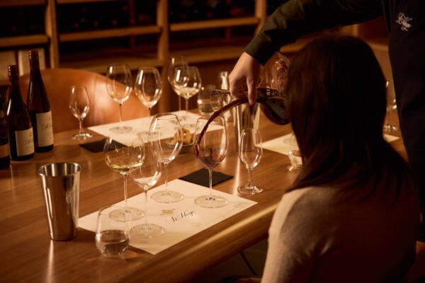 4 wineglasses on table with a lady waiting to taste red wine.